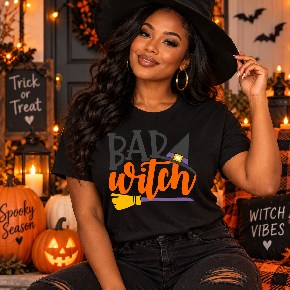 Black Halloween T-shirt featuring a “Bad Witch” graphic with orange lettering, witch hat, and broom, modeled by a woman in a spooky Halloween setting.
